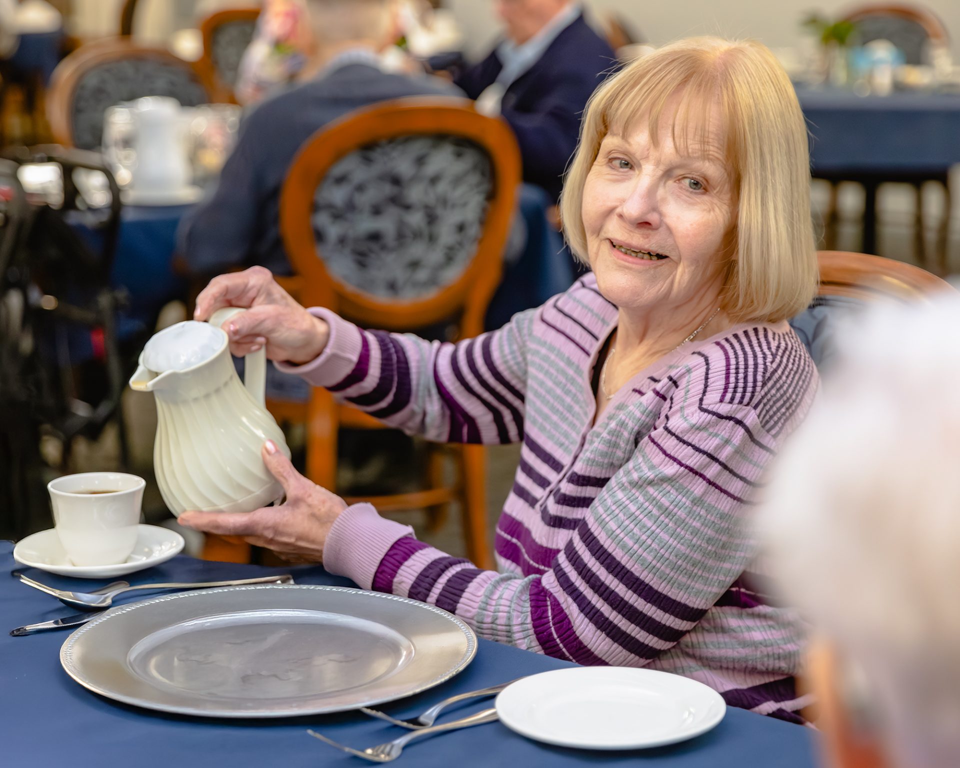 Resident enjoys pouring tea during a social gathering at Gardens Retirement Living, showcasing the life-enriching activities